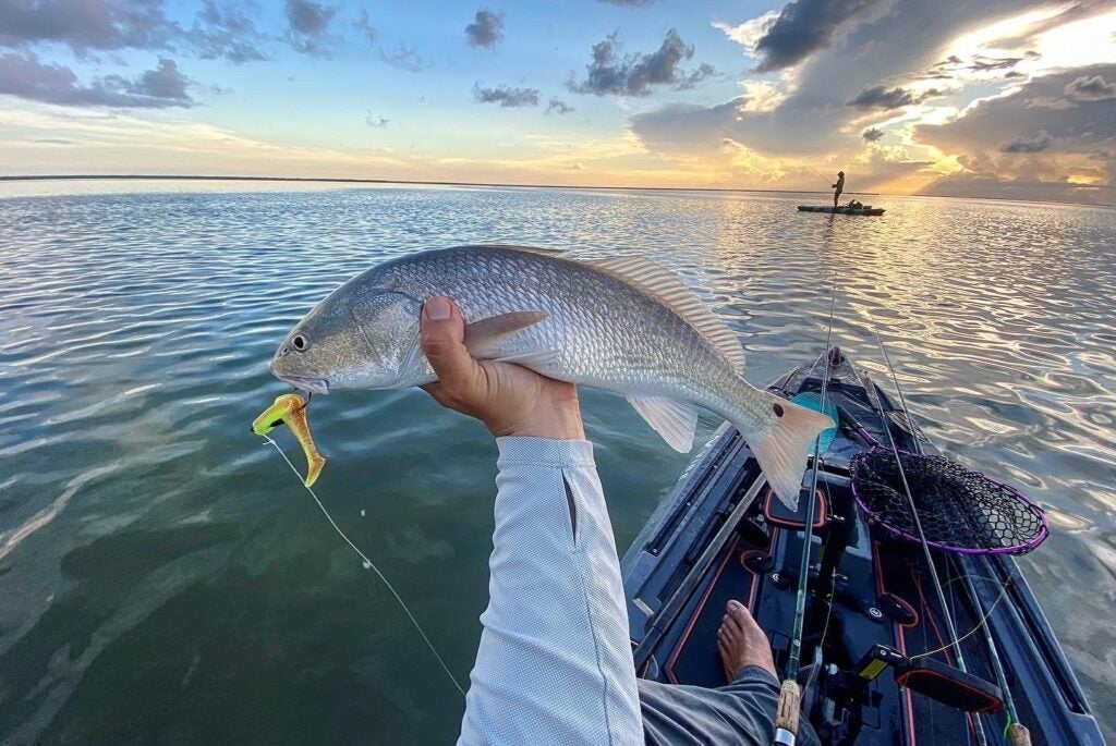 A person holding a fish out toward the sunset over a body of water