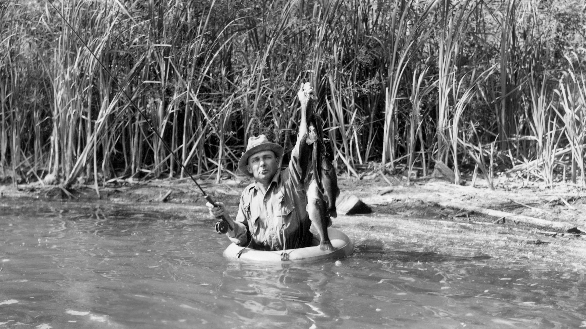 near-shore angler in small inner tube holds up stringer of fish