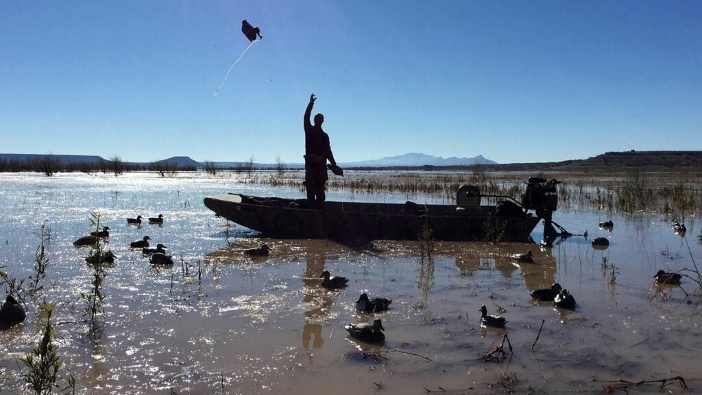 A hunter stands on a boat while scanning the sky for waterfowl.