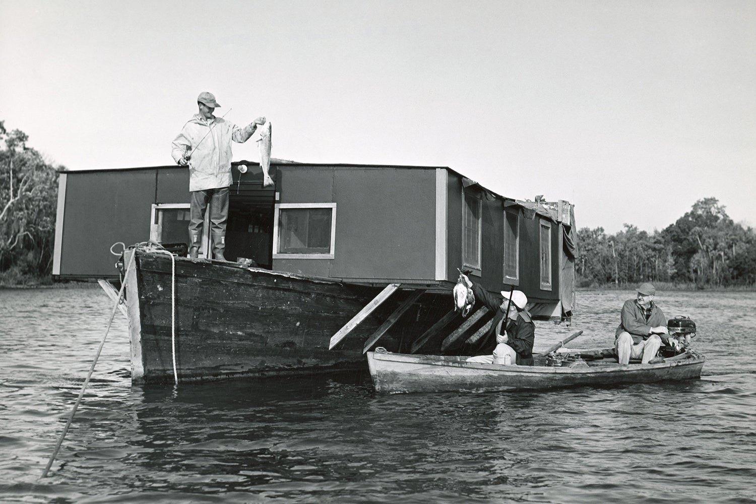 angler shows off redfish from bow of boat that has unusual house-like structure on top of it; two anglers in smaller boat have pulled up alongside with freshly killed ducks