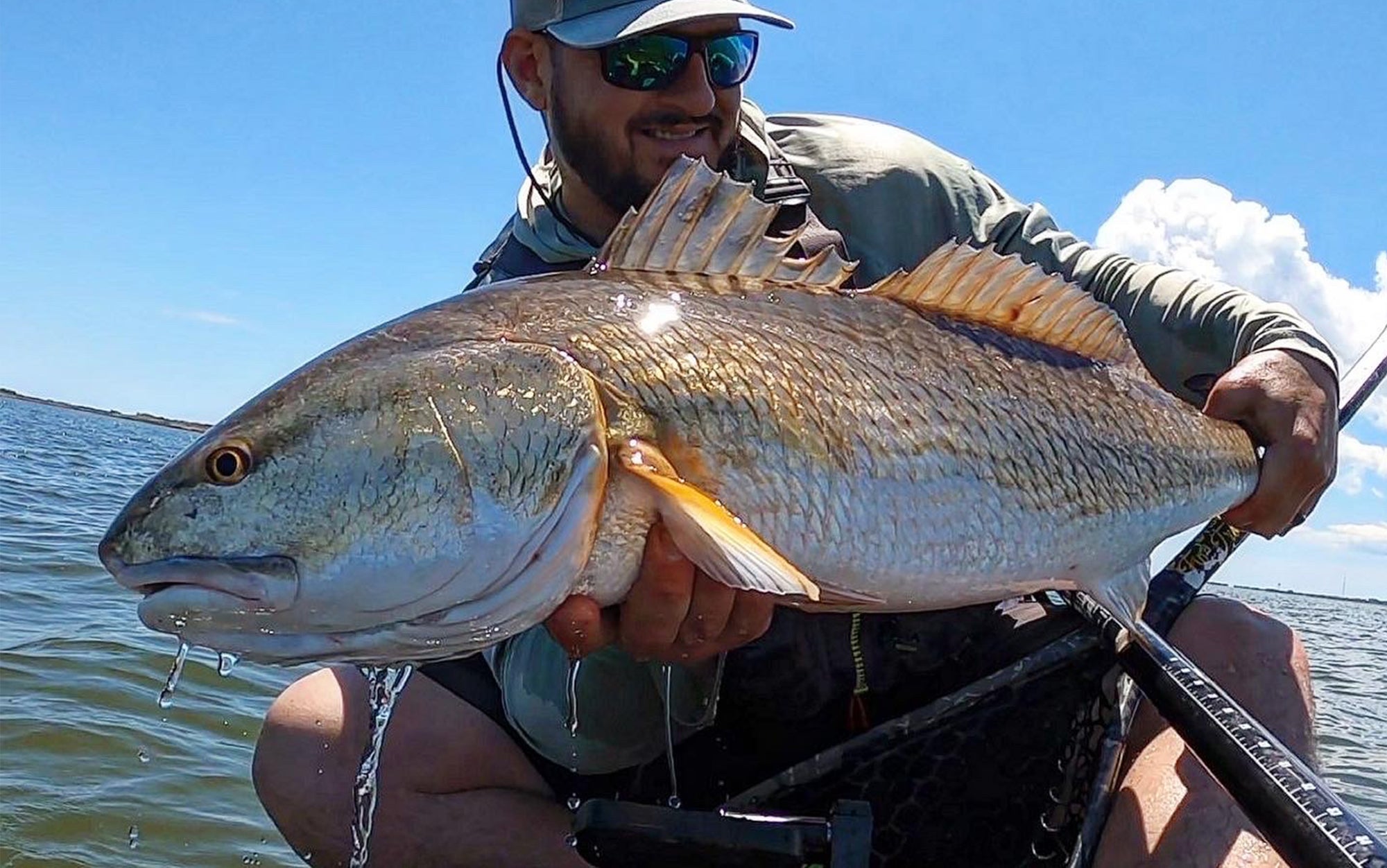 Angler poses with fish on kayak.
