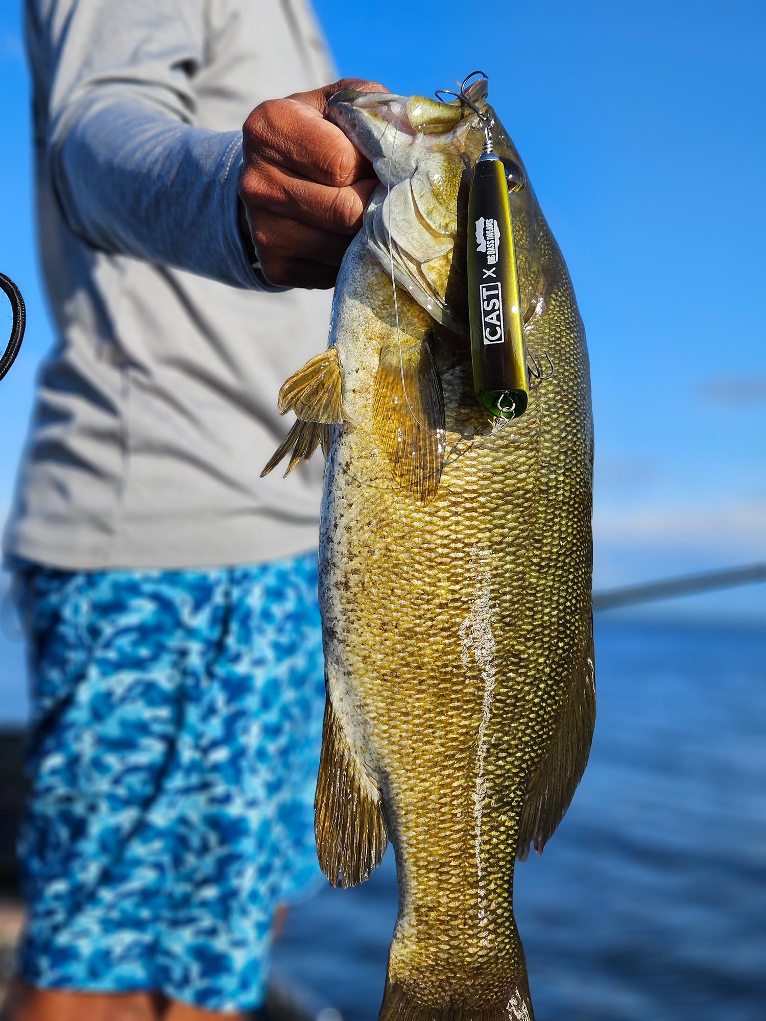 angler holds largemouth by lip as lure dangles from its mouth