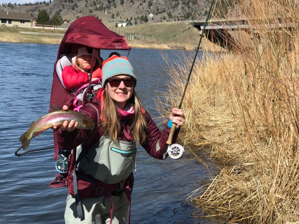 A woman fishing with a toddler in a red backpack