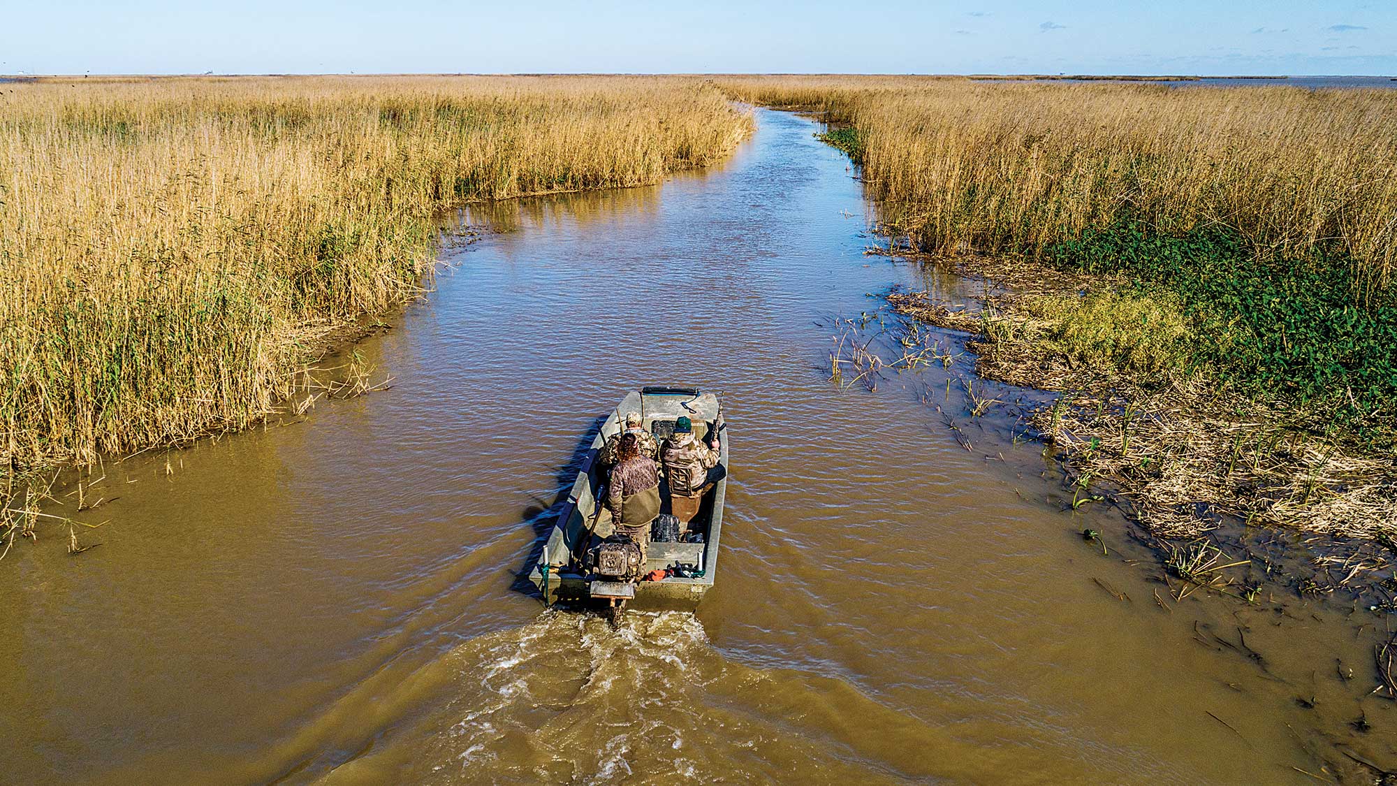boat moves through up muddy river in marshy area with destroyed vegetation on the right