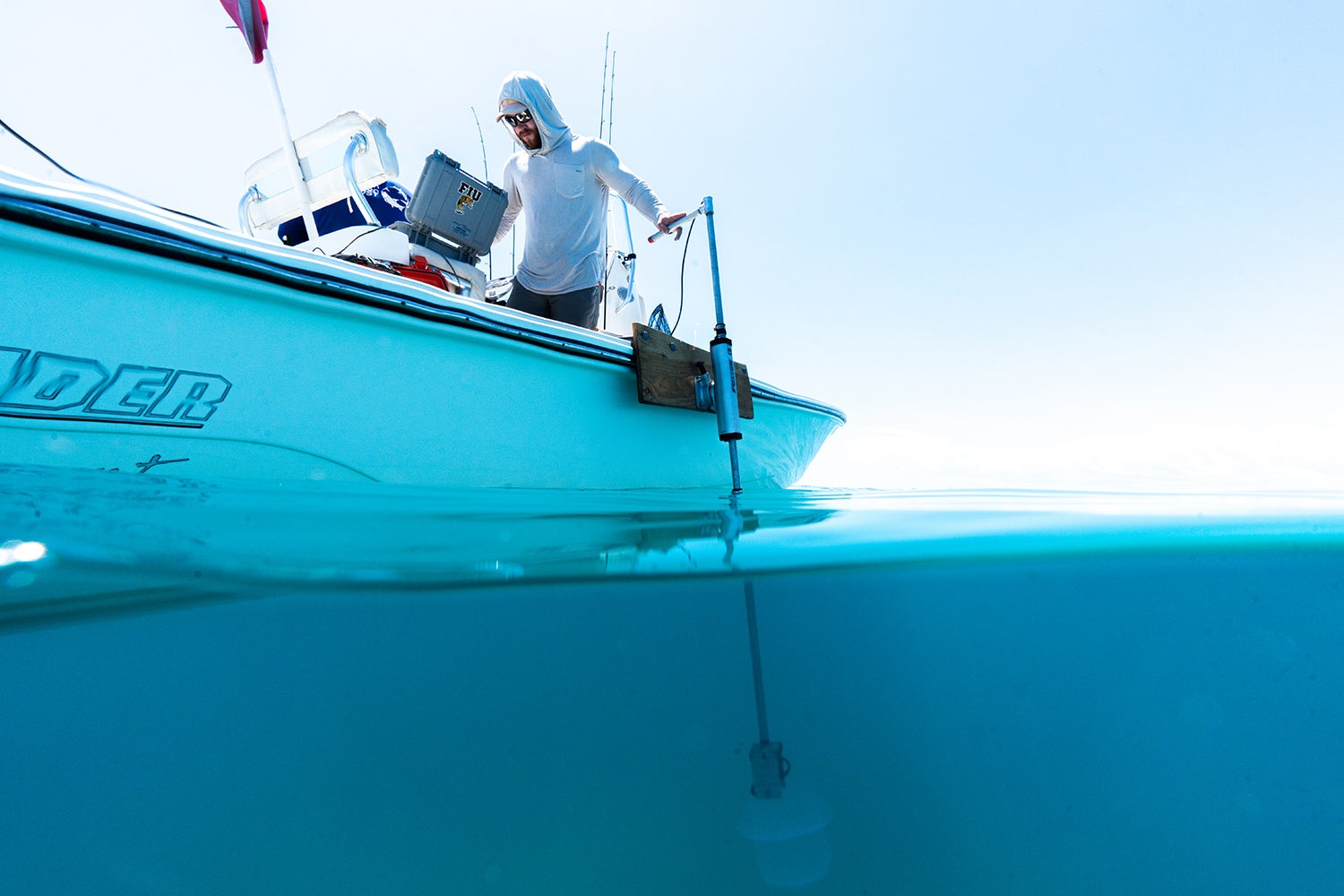 researcher on boat has hand on top of hydrophone, which stretches down into water below boat