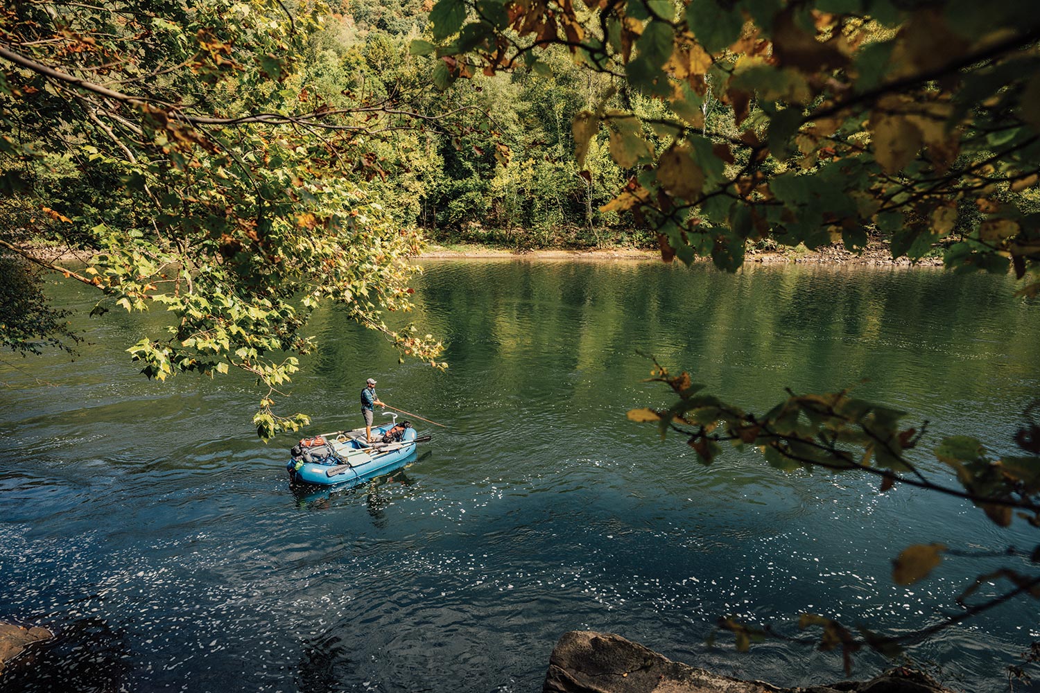 Angler standing on raft casts into calm section of river.