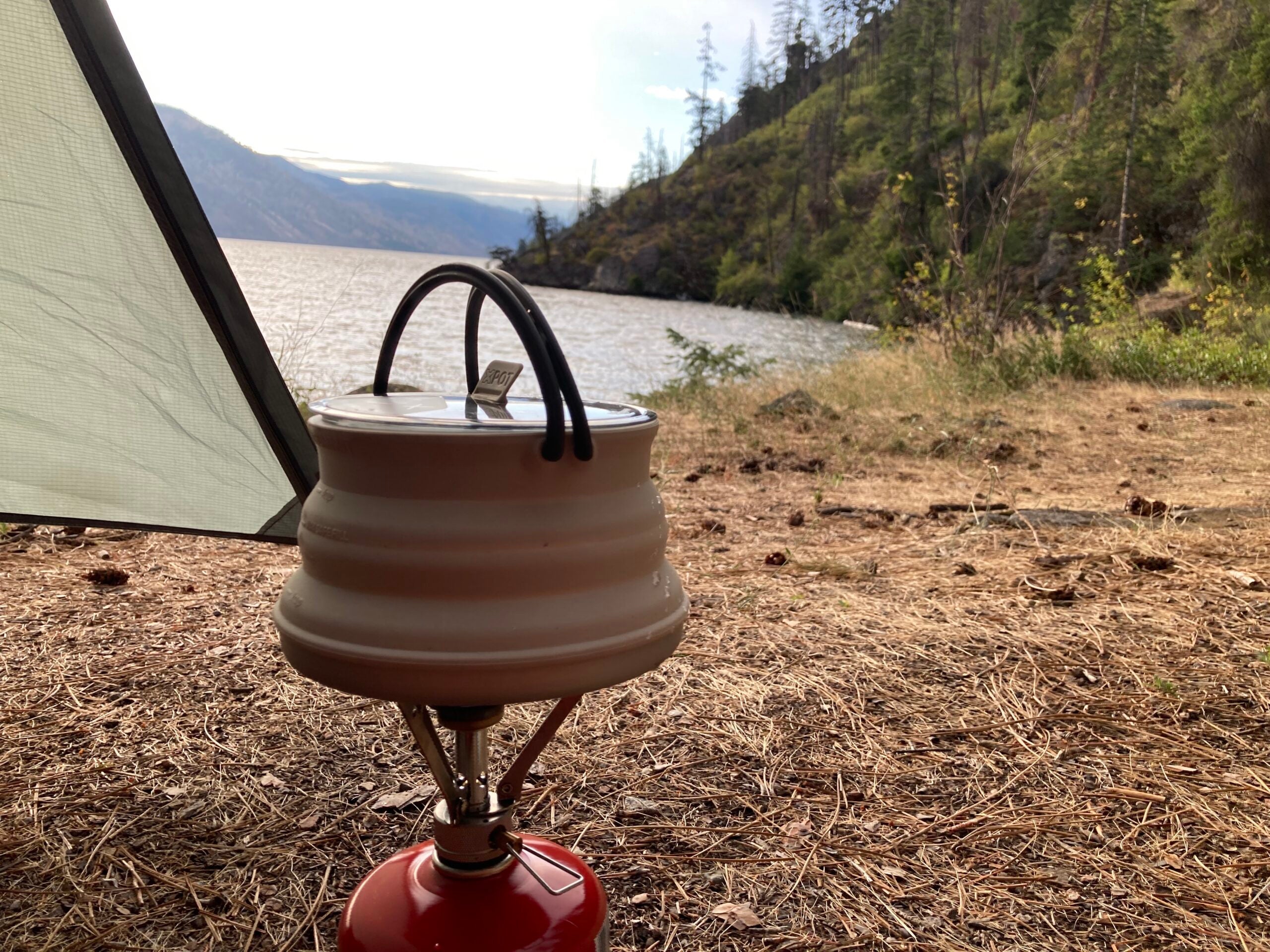 A pot of tea boiling over a camping stove at a camp site.