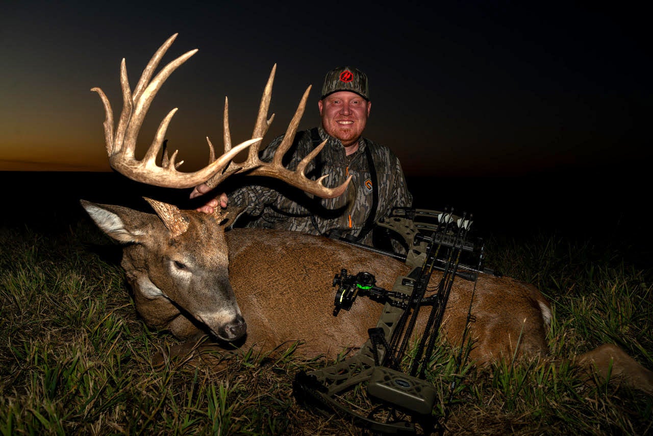 A Missouri hunter poses behind a 190-class whitetail buck in a field after dark.