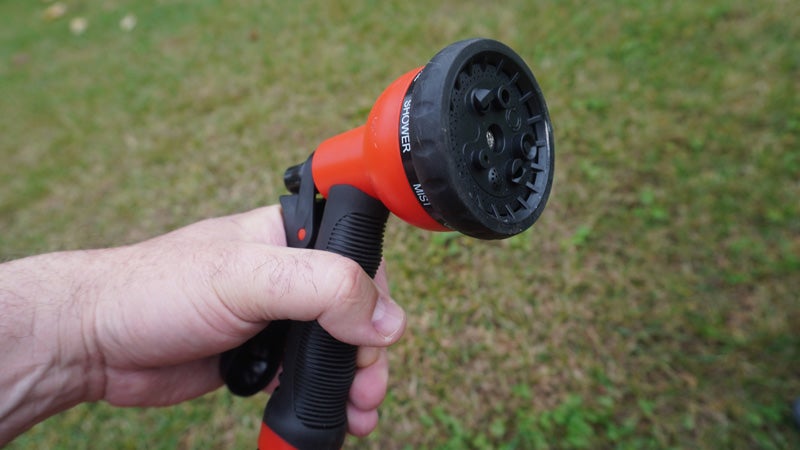 The red and black nozzle of a hydropod shower being held in front of a green grass background.
