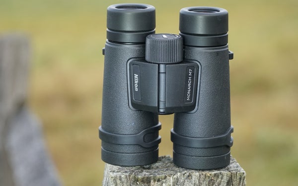 Nikon Monarch M7 10x42 binocular sitting on a fence post with a field in background.
