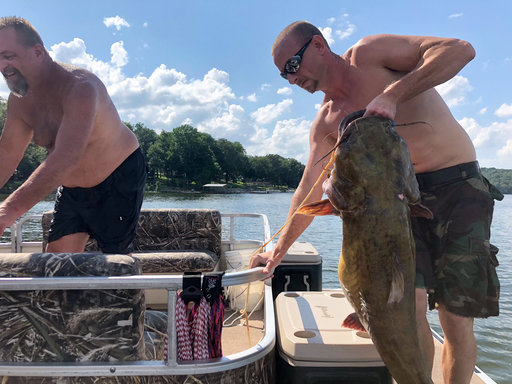 A man holds up a flathead on a pontoon boat.