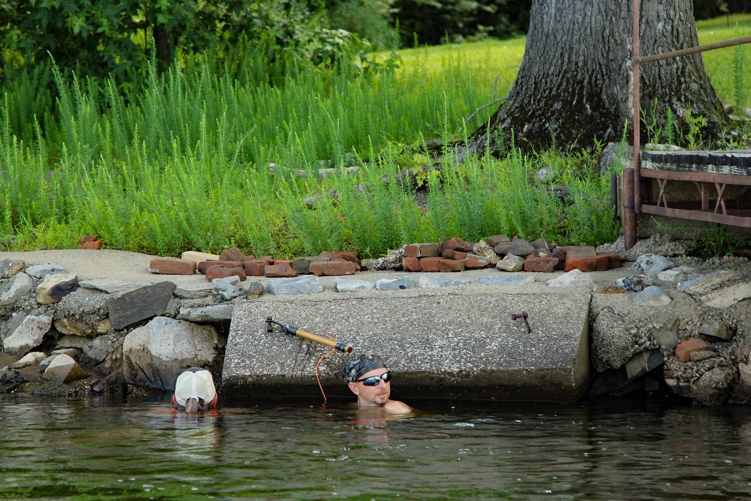 Two noodlers check concrete slab for catfish.