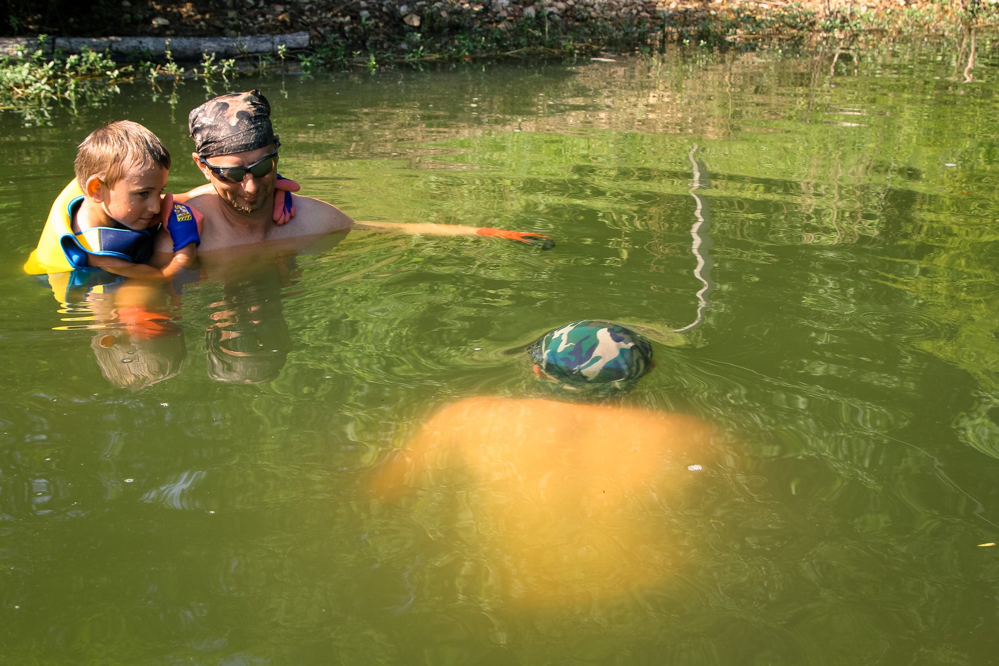 A noodler checks a catfish hole while his buddy looks on.