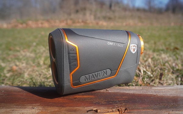 An orange and gray Maven CRF.1 rangefinder sitting on a log in a grassy field.