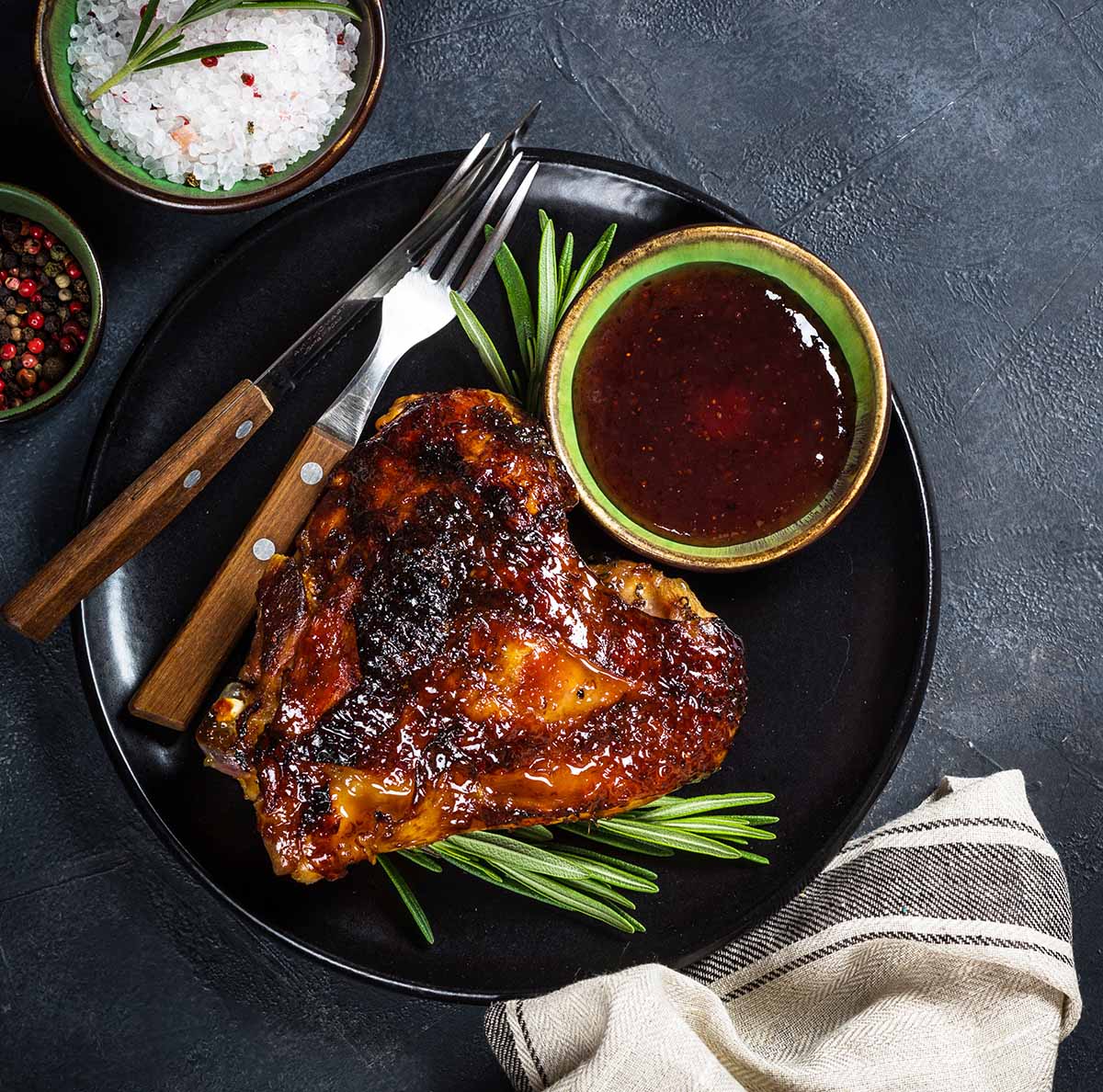 A barbecued turkey thigh on a plate with sauce. 